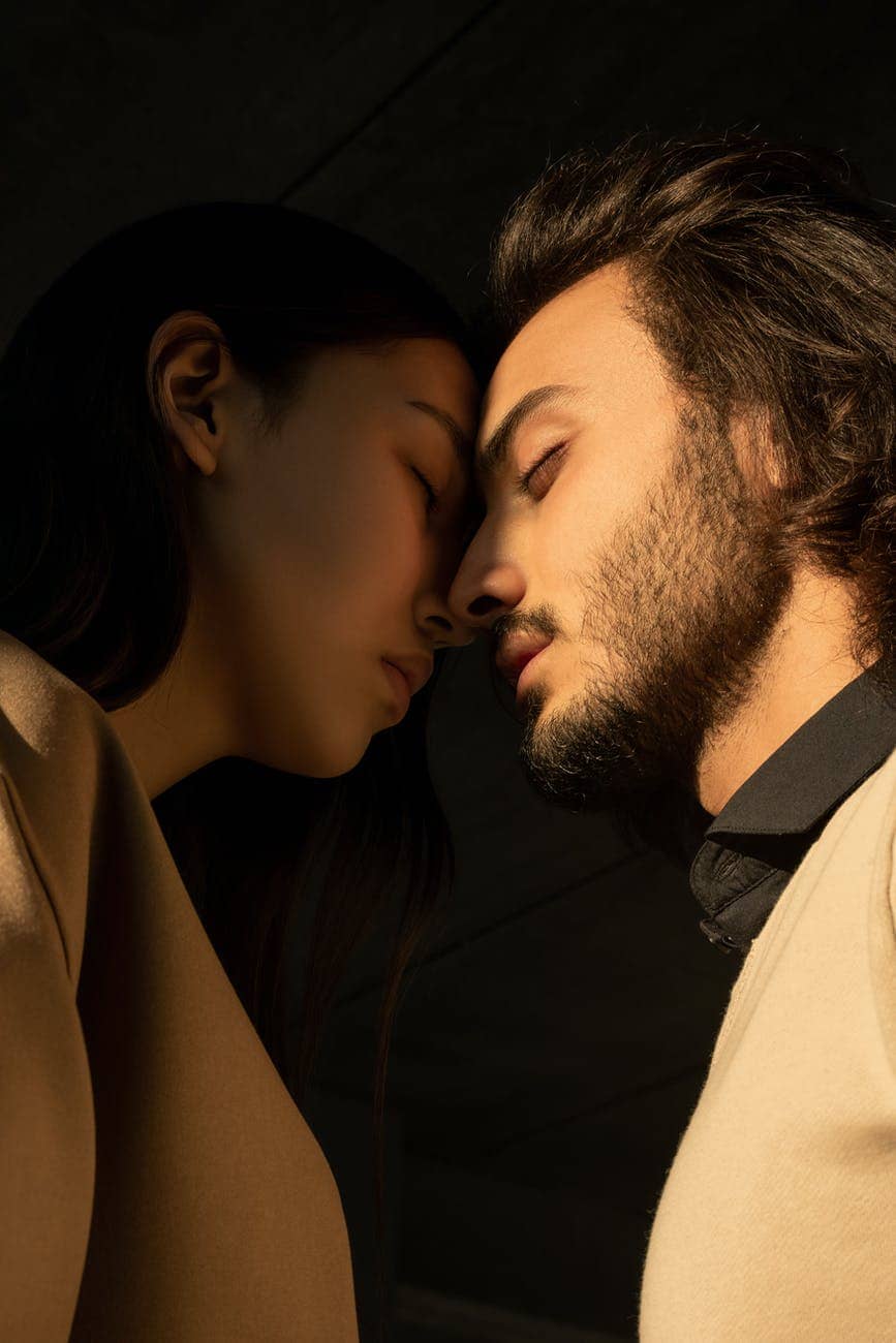 close up photo of couple with their eyes closed facing each other in front of dark background